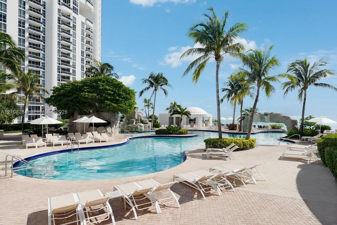 Resort-style swimming pool featuring rock waterfall features, paver decking, and integrated landscaping