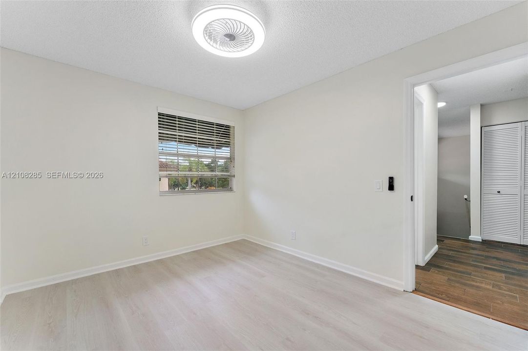 Interior space featuring neutral wall paint, wood-finish flooring, a recessed window with horizontal blinds, and a circular LED flush-mount ceiling fixture
