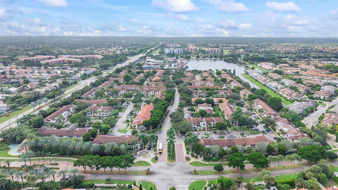 Aerial perspective featuring a residential community with paved roadways, tile-roofed structures, mature landscaping, and proximity to a central water feature