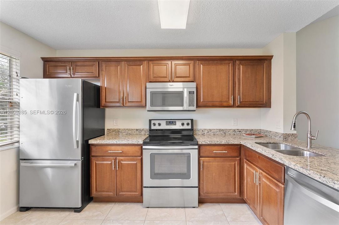 Kitchen featuring wooden cabinetry, stone-surface countertops, stainless steel appliances, a double-basin sink with a pull-down faucet, and tiled flooring