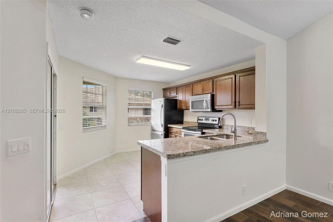 Kitchen featuring stone-finish countertops, stainless steel appliances, wood-finish cabinetry, and ceramic tile flooring