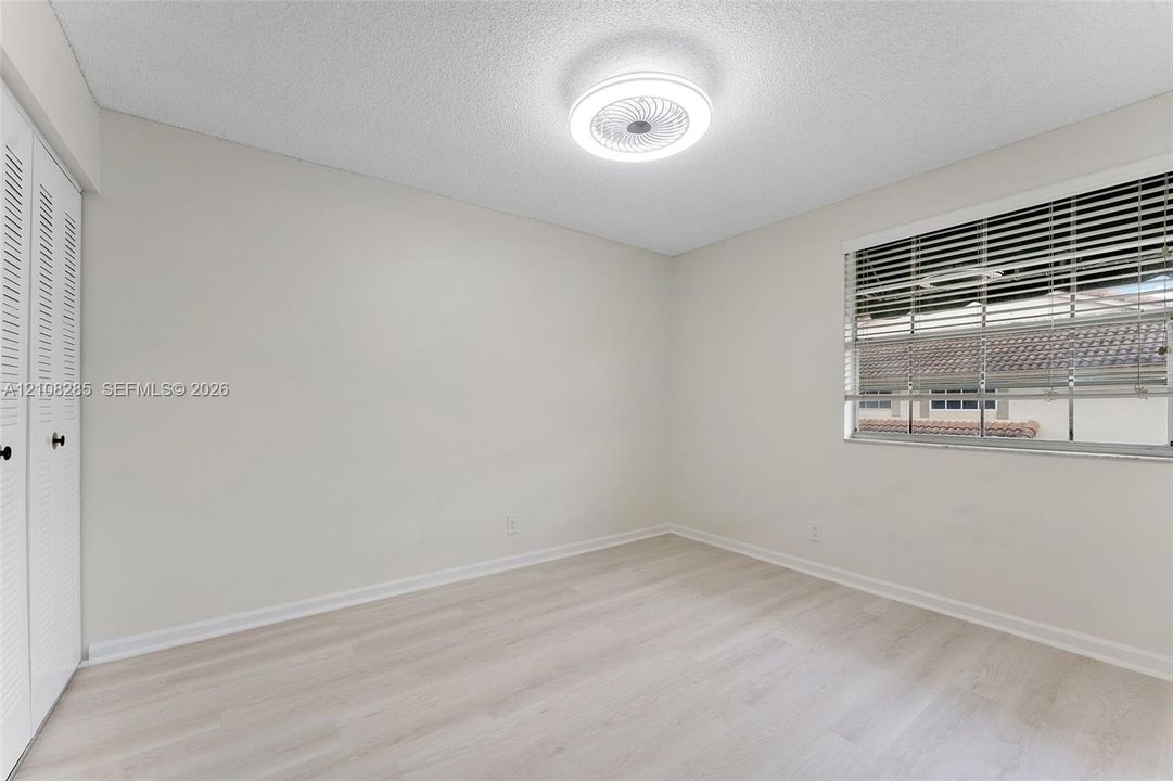 Light-toned wood-finish flooring, ceiling-mounted LED light fixture, double-door closet with louvered panels, and horizontal window blinds