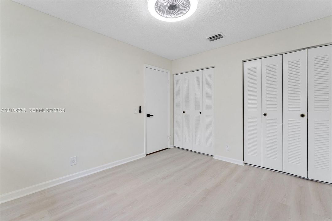 Neutral-toned room featuring wood-finish flooring, dual closets with louvered doors, and a central circular flush-mount ceiling light