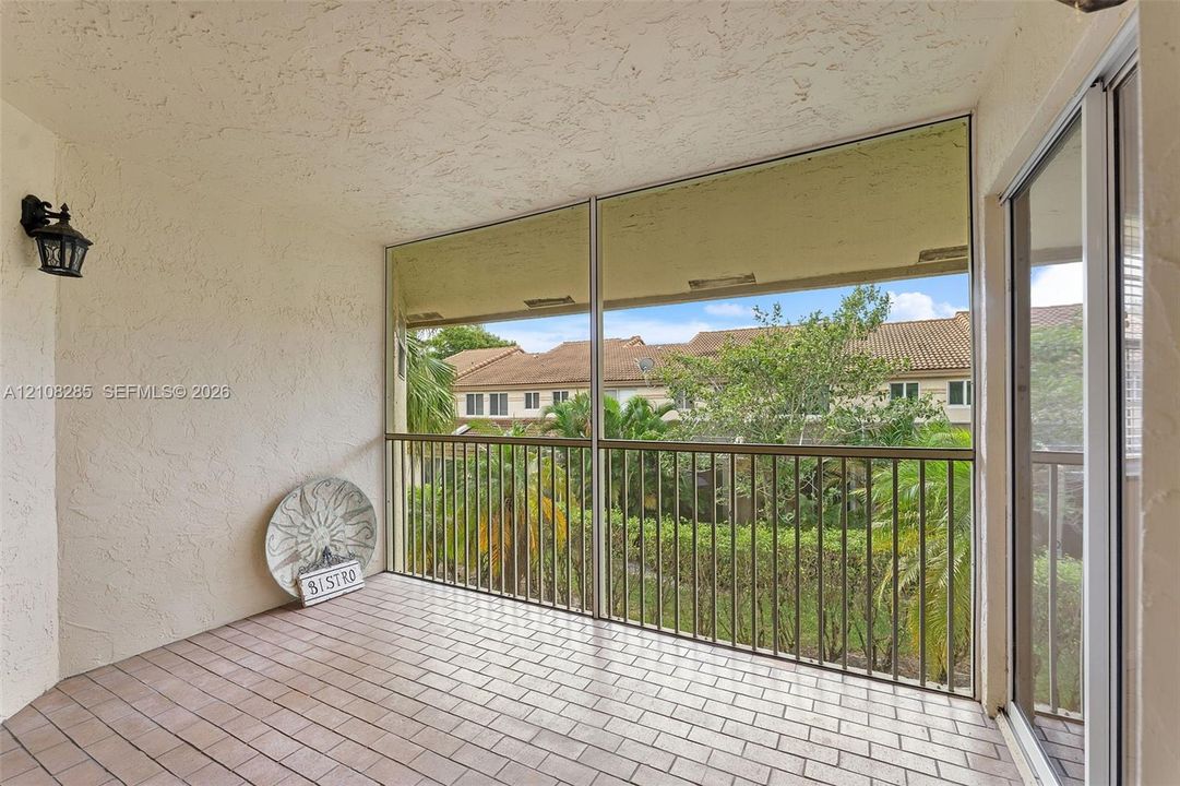 Covered balcony featuring tile flooring, metal railings, a screened enclosure, and wall-mounted exterior lighting