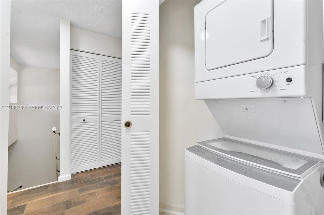 Stacked laundry unit featuring white cabinetry, louvered closet doors, and wood-finish flooring