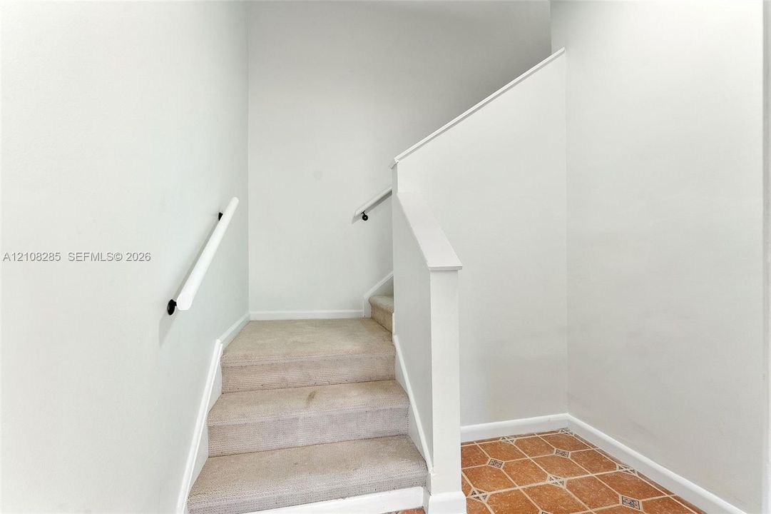 Staircase with neutral-toned carpeting, white railings, and terracotta-style tile flooring