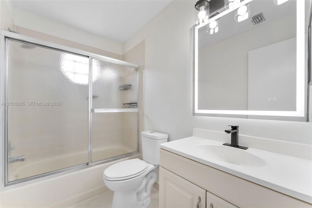 Bathroom featuring a vanity with a white countertop and oval under-mount sink, matte black faucet, LED-backlit mirror, and a tub-shower combination with a sliding glass enclosure