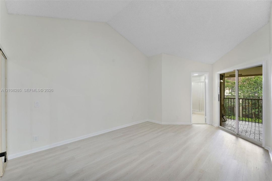 Vaulted ceilings, wood-finish flooring, and sliding glass doors with exterior balcony access