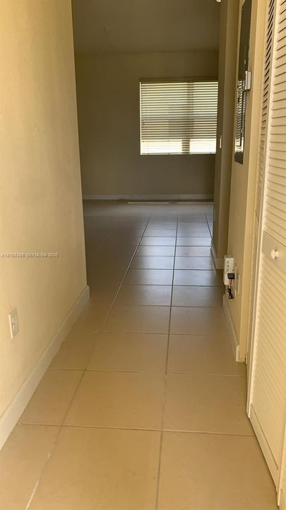 Interior corridor featuring neutral-toned tile flooring and a built-in louvered closet door