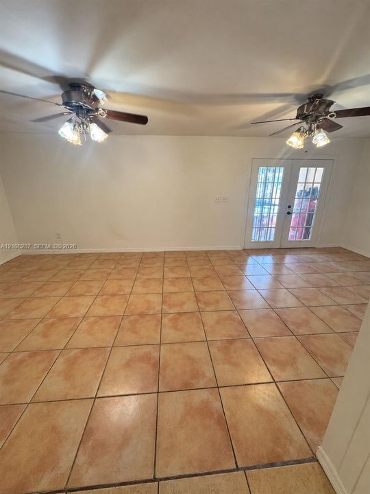 Large-format neutral tile flooring throughout, dual ceiling fans with multi-light fixtures, and white-paned French doors