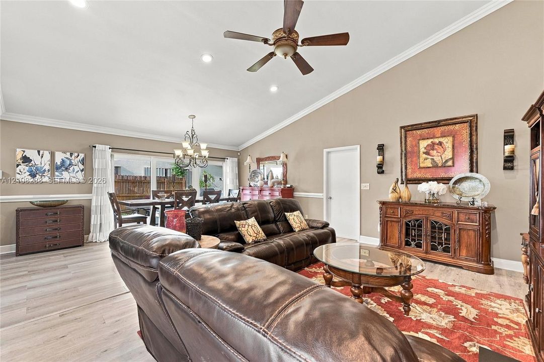 Living area featuring a vaulted ceiling, wood-finish flooring, crown molding, chair rail trim, and a ceiling fan