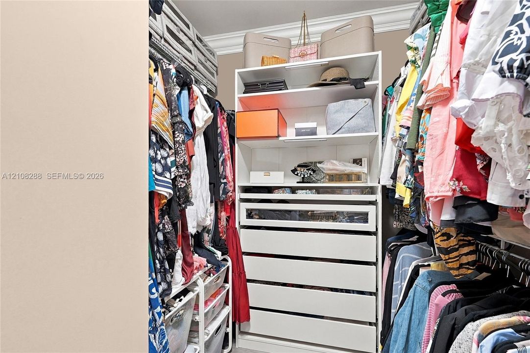 Walk-in closet featuring white built-in cabinetry, floor-to-ceiling storage, a glass-front display drawer, and crown molding