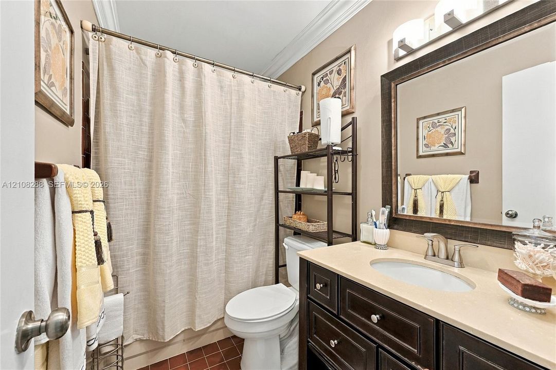 Guest Bathroom featuring a vanity with dark-finish cabinetry, a light-toned countertop, and an undermount oval sink, complemented by a framed wall mirror, crown molding, and tiled flooring