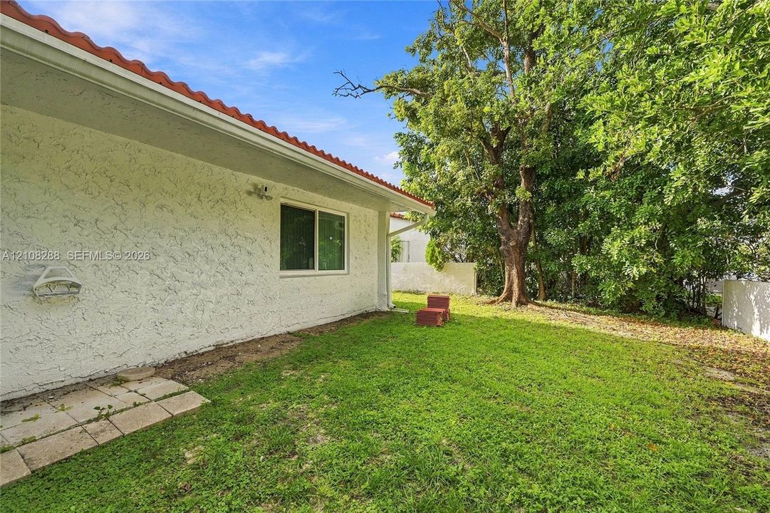 Exterior side yard featuring textured stucco walls, a red-tile roof, a single-pane sliding window, and mature trees