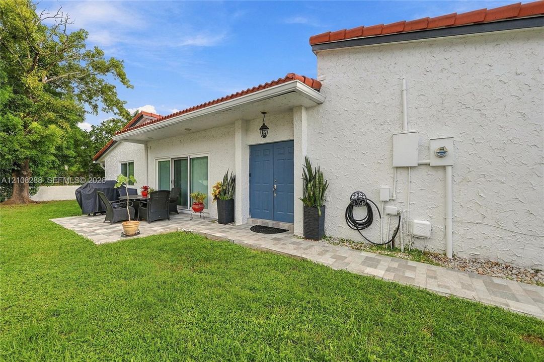 Stucco exterior featuring a dual-tone tile roof, blue double entry doors, and expansive paver patio hardscaping