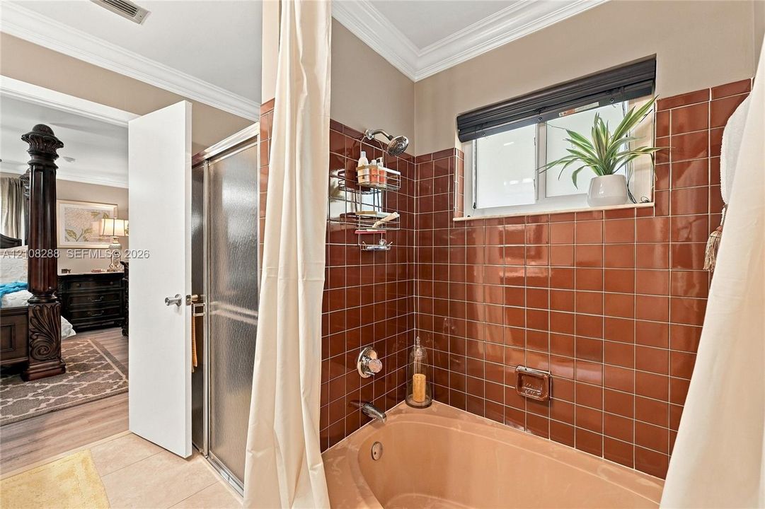 Bathroom featuring a sunken cultured marble Roman tub, floor-to-ceiling high-gloss terracotta wall tile, integrated shower enclosure with a frosted glass door, and a horizontal window with a dark trim finish