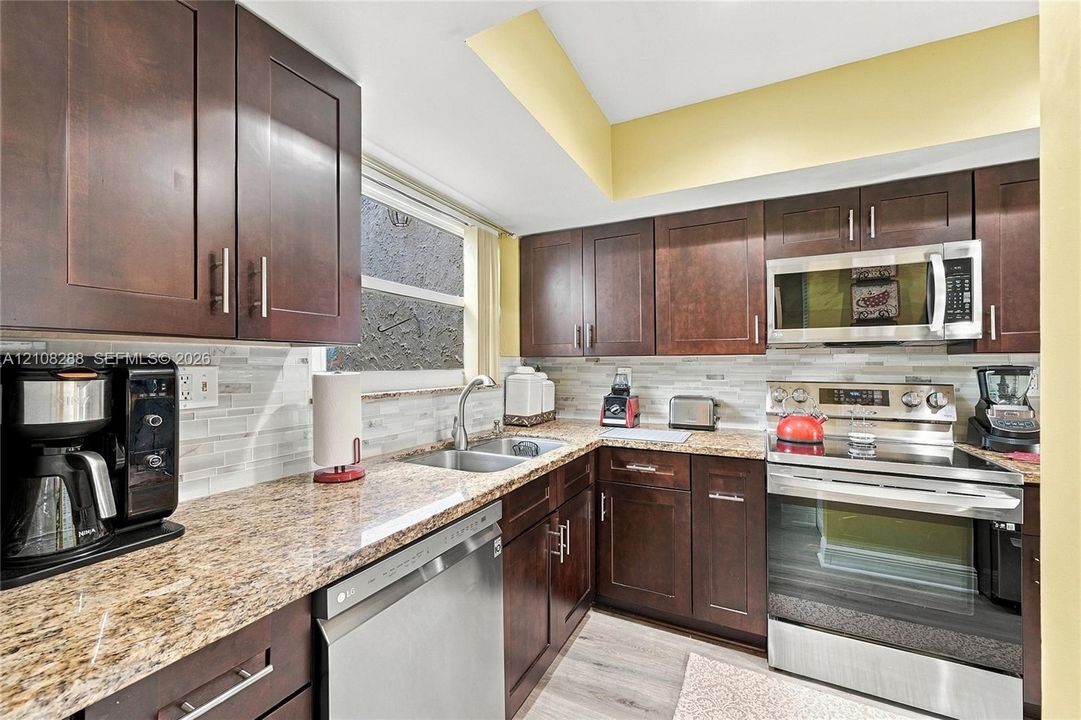 Kitchen featuring dark-toned cabinetry, stone-finish countertops, stainless steel appliances, light-toned horizontal tile backsplash, and light-toned hard-surface flooring