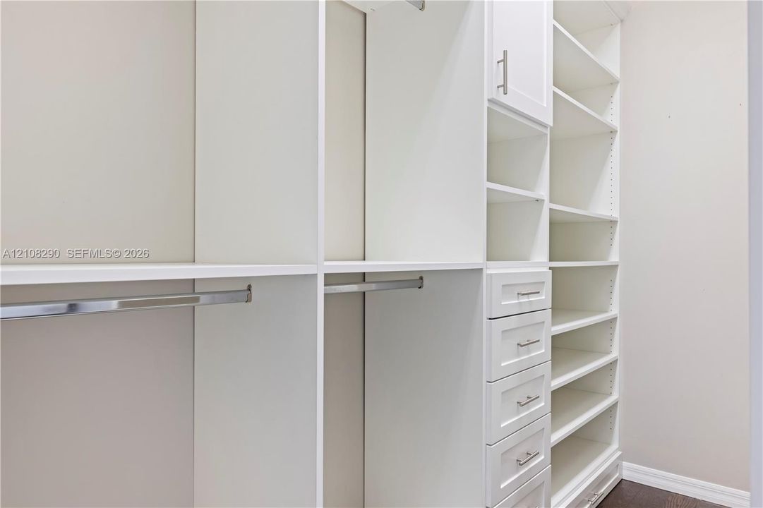 Custom closet featuring floor-to-ceiling white cabinetry, built-in shelving, integrated hanging rods, and a bank of storage drawers with brushed metal pulls