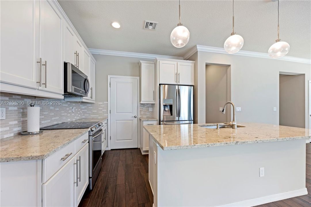 Kitchen featuring white shaker-style cabinetry, stone countertops, stainless steel appliances, decorative glass pendant lighting, and wood-finish flooring