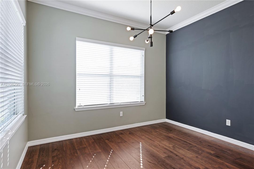 Room featuring wood-finish flooring, a dark accent wall, crown molding, and a contemporary multi-arm chandelier
