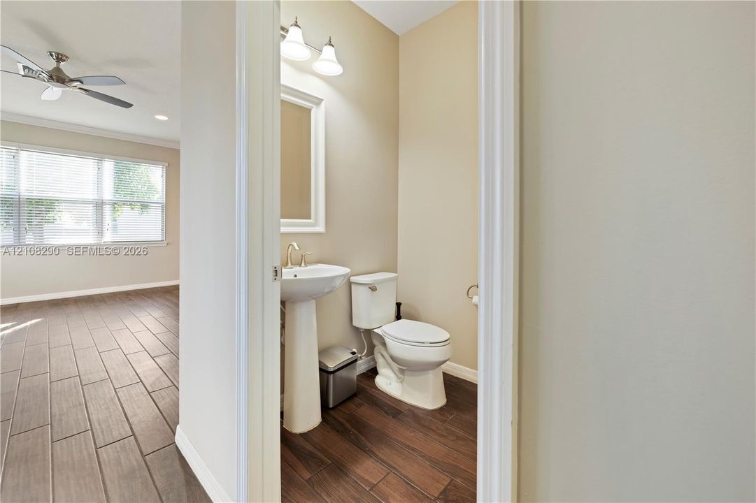 Pedestal sink with a polished metal faucet, multi-light fixture, white toilet, and wood-finish tile flooring