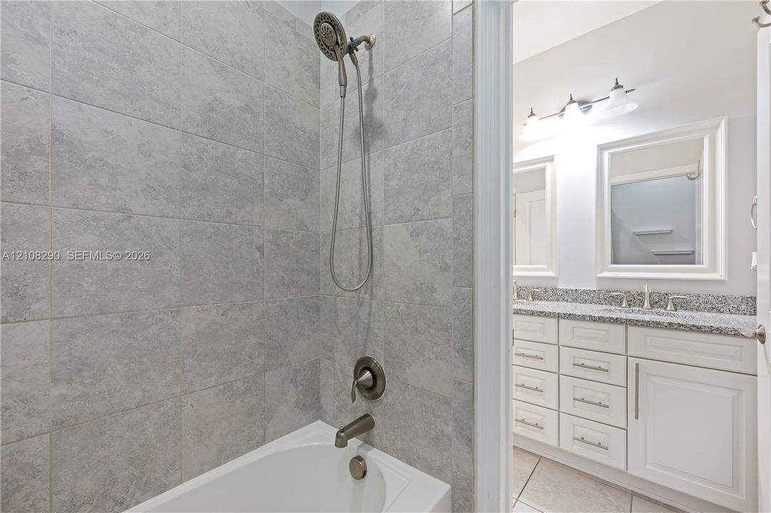 Shower area featuring stone-look wall tile and a multi-setting handheld showerhead