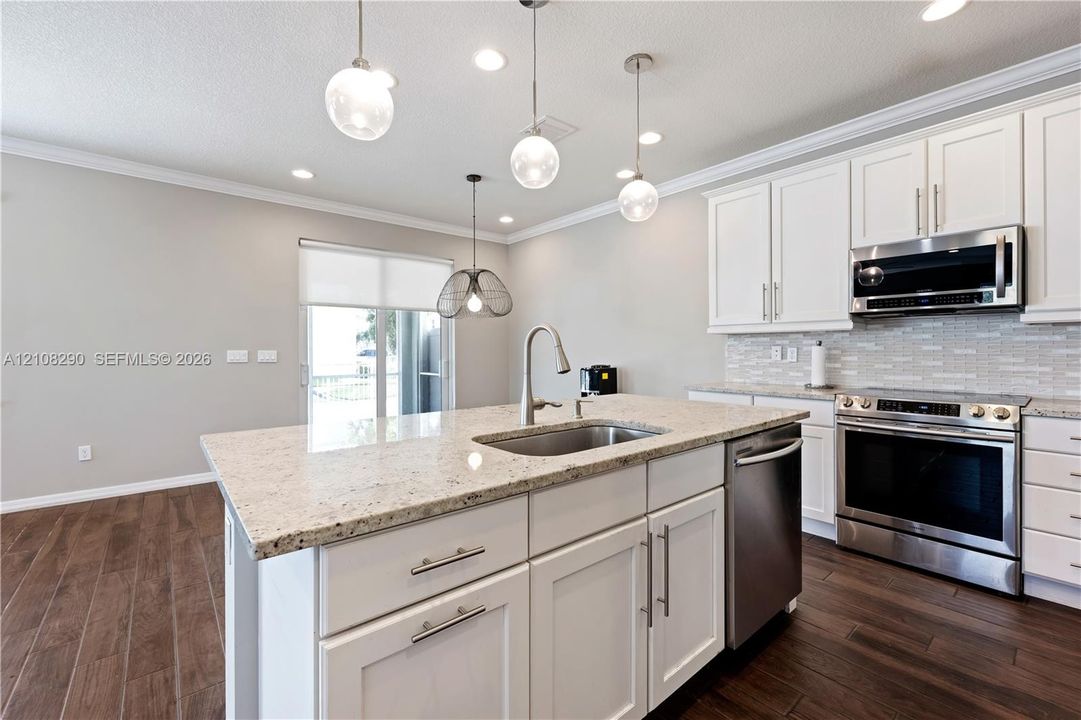 Kitchen featuring white shaker-style cabinetry, stone countertops, stainless steel appliances, wood-finish flooring, and multi-pendant lighting
