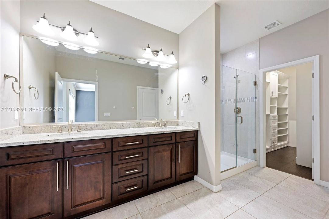 Double vanity featuring dark wood-finish cabinetry, stone-surface countertop, dual undermount sinks, and a large-format vanity mirror with dual light fixtures