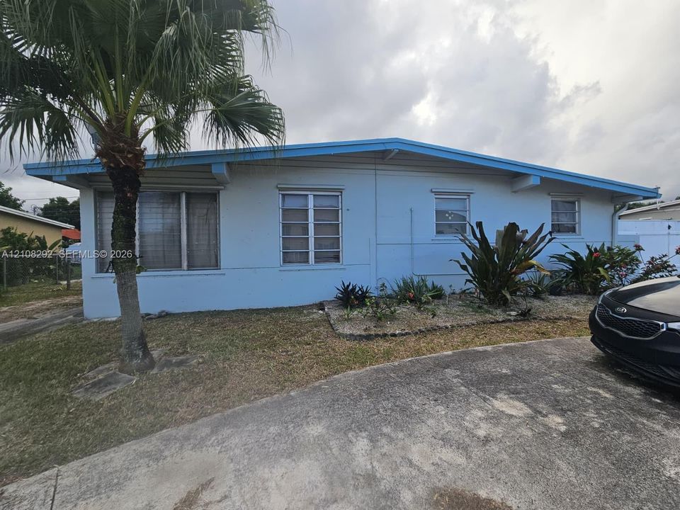 Single-story exterior featuring light blue siding, a low-pitch roofline, exposed rafter tails, metal-frame windows, and a concrete driveway