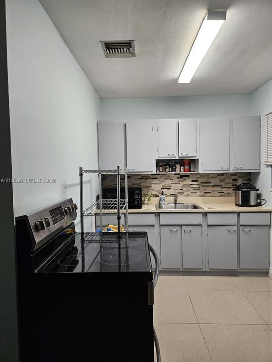 Kitchen featuring gray cabinetry, a multi-tone tile backsplash, a stainless steel sink with a mounted faucet, and large-format floor tiling