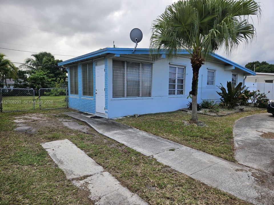 Exterior featuring painted brick siding, multi-pane windows, a concrete driveway, a paved walkway, and an enclosed chain-link fenced lot