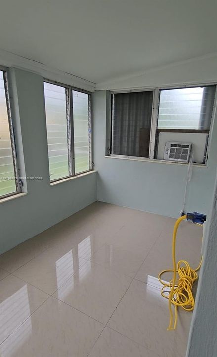 Enclosed space featuring large format light-toned tile flooring, light-colored wall paint, and multiple louvered windows