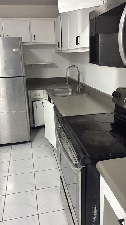 Kitchen featuring white cabinetry, stainless steel appliances, solid-surface countertops, a stainless steel sink with a high-arch faucet, and tile flooring