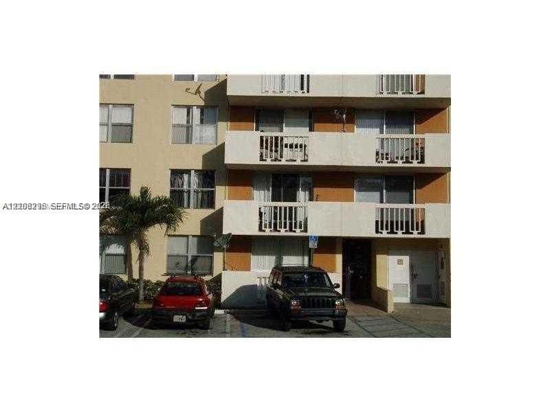 Multi-story exterior facade featuring concrete balconies with vertical railings, stucco finish, grid-pattern windows, and exterior parking