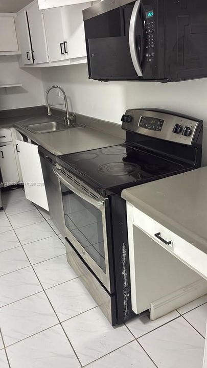 Kitchen featuring white cabinetry, stainless steel microwave, black electric range with stainless steel trim, solid-surface countertops, and tiled flooring