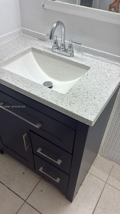 Bathroom vanity featuring a dark-finish cabinet with satin nickel hardware, a speckled composite countertop, an integrated rectangular sink, and a high-arc chrome faucet