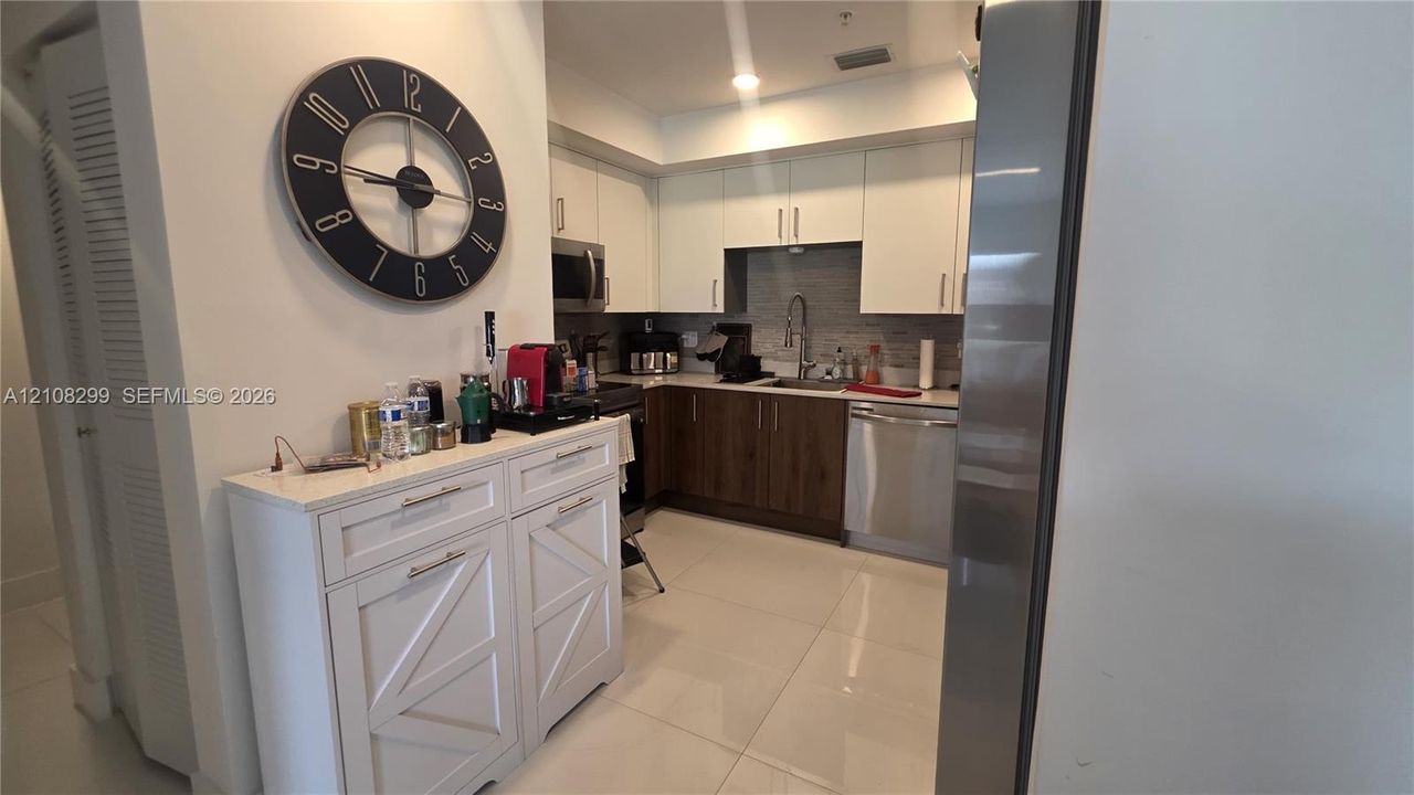Kitchen featuring two-tone cabinetry with white upper and wood-finish lower units, stainless steel appliances, stone-composite countertops, and a tiled backsplash