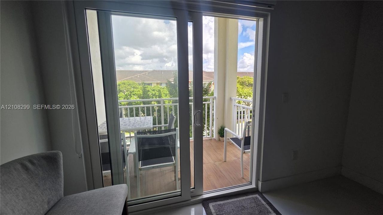 Glass sliding door opening to a private balcony with wood-finish decking and white metal railings