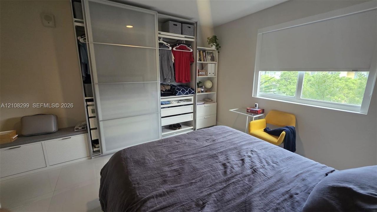 Built-in floor-to-ceiling wardrobe featuring sliding frosted-glass doors, integrated shelving, and drawers, accompanied by a low-profile storage bench and large-format tile flooring