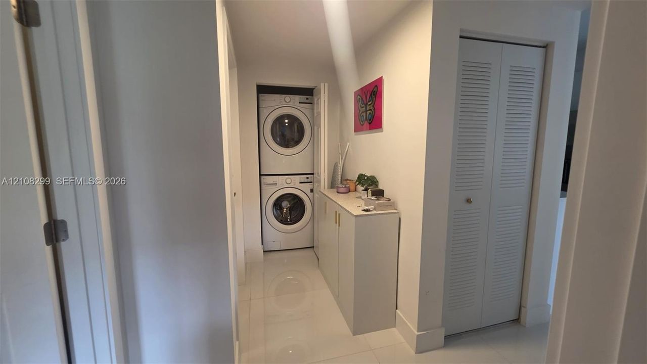 Utility area featuring a stacked washer and dryer, built-in cabinetry with flat-panel doors, and polished flooring