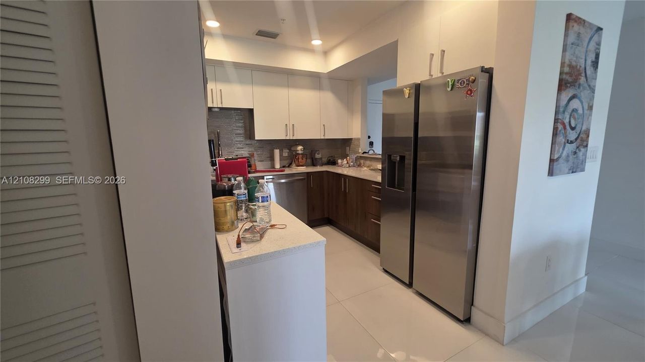 Kitchen featuring flat-panel two-tone cabinetry, quartz countertops, stainless steel appliances, and large-format tile flooring
