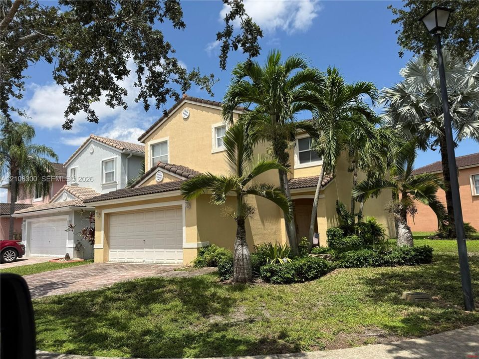 Stucco exterior residence featuring a two-car garage, pitched tile roof, and mature palm tree landscaping