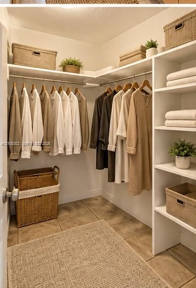 Walk-in closet featuring white built-in shelving, integrated closet rods, and neutral tile flooring