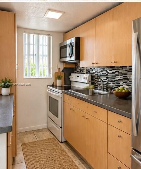 Kitchen featuring flat-panel wood cabinetry, dark solid-surface countertops, mosaic tile backsplash, and stainless steel appliances