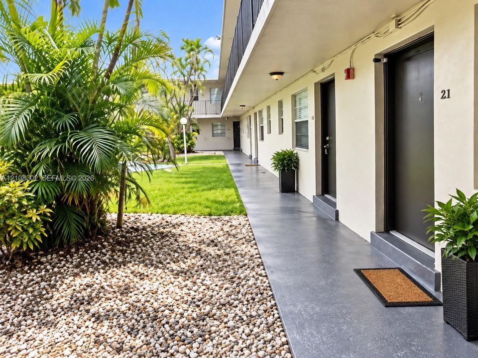 Exterior walkway featuring a concrete surface, overhead flush-mount lighting, and access to units