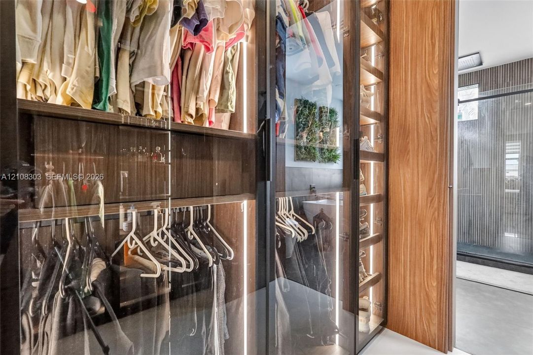 Custom closet system featuring floor-to-ceiling glass panel doors, integrated vertical LED lighting, wood-finish cabinetry, and built-in shelving