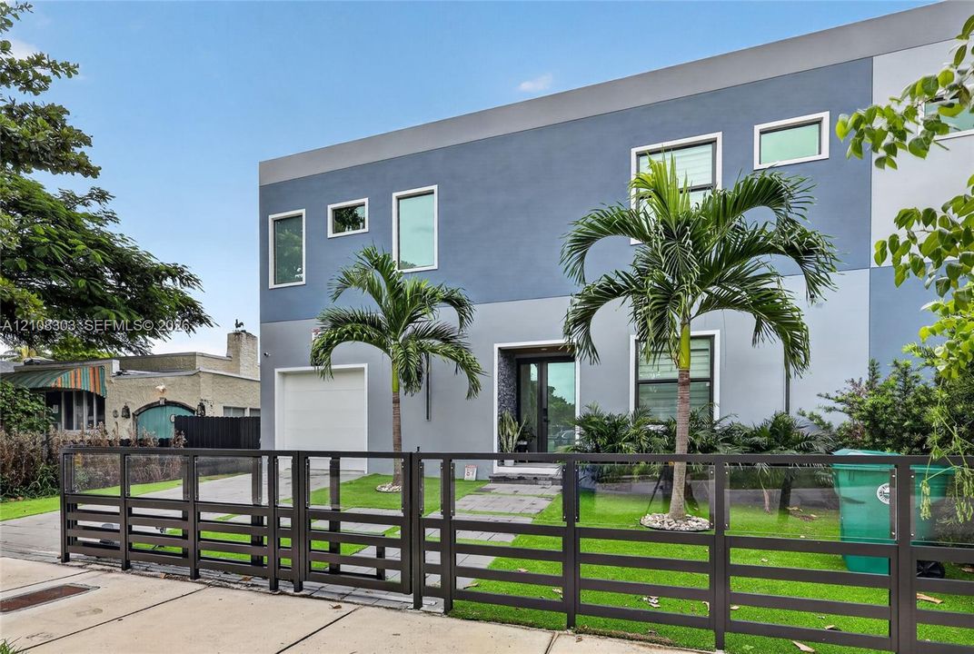 Modern two-story exterior featuring multi-tonal gray stucco finish, clean-lined horizontal metal fencing, a paved front walkway, and an attached single-car garage