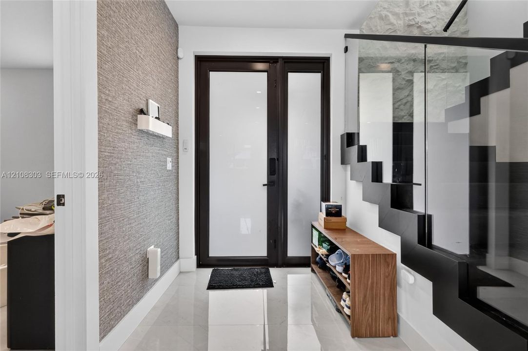 Entryway featuring a black-framed glass entry door, large-format tile flooring, textured wall covering, and a staircase with open risers and a glass railing