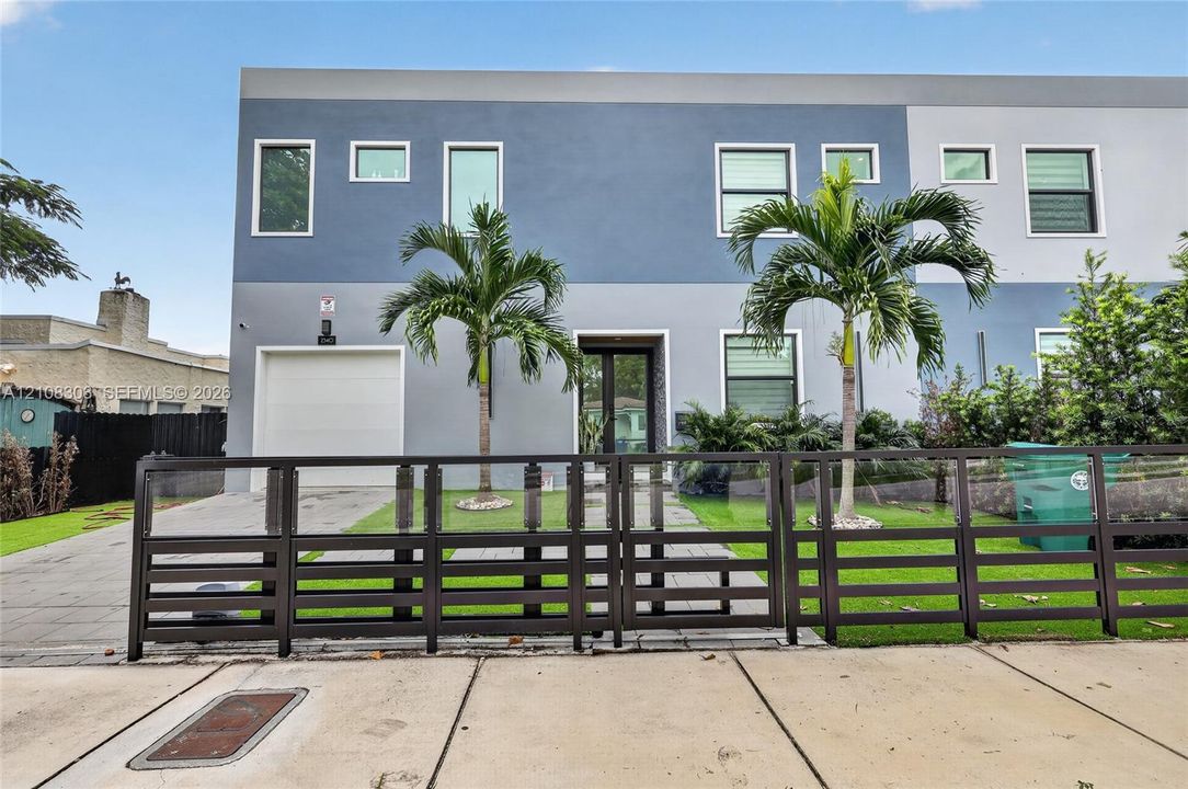 Modern two-story exterior featuring multi-tonal stucco facade, horizontal slat metal fencing, integrated single-car garage, and paved walkway