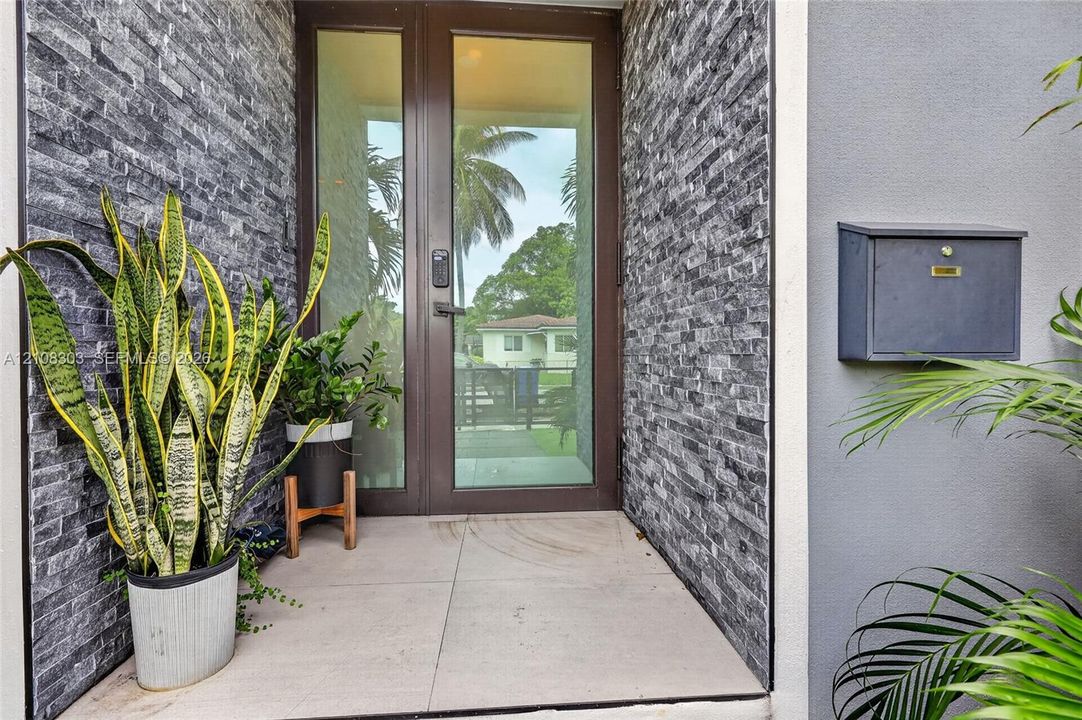 Entryway featuring a full-glass door with dark metal frame, charcoal-toned stacked stone accent walls, large-format tile flooring, and a wall-mounted metal mailbox